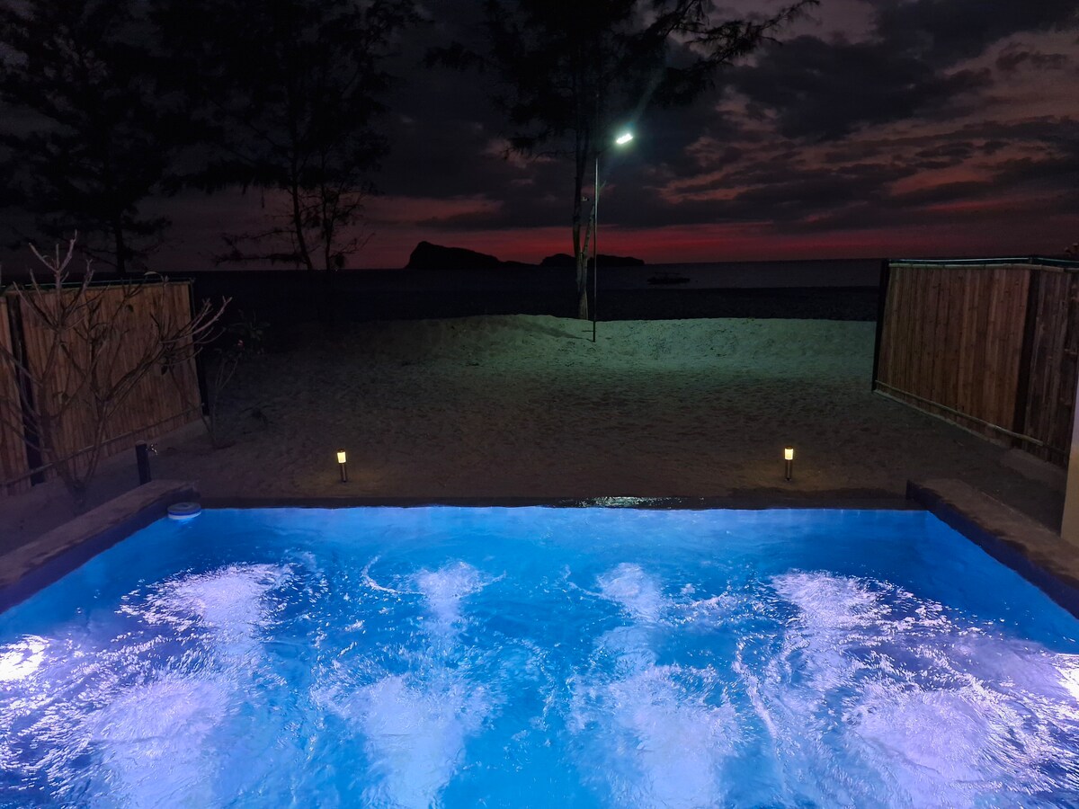 Nighttime view of illuminated pool with spa jets and beach beyond