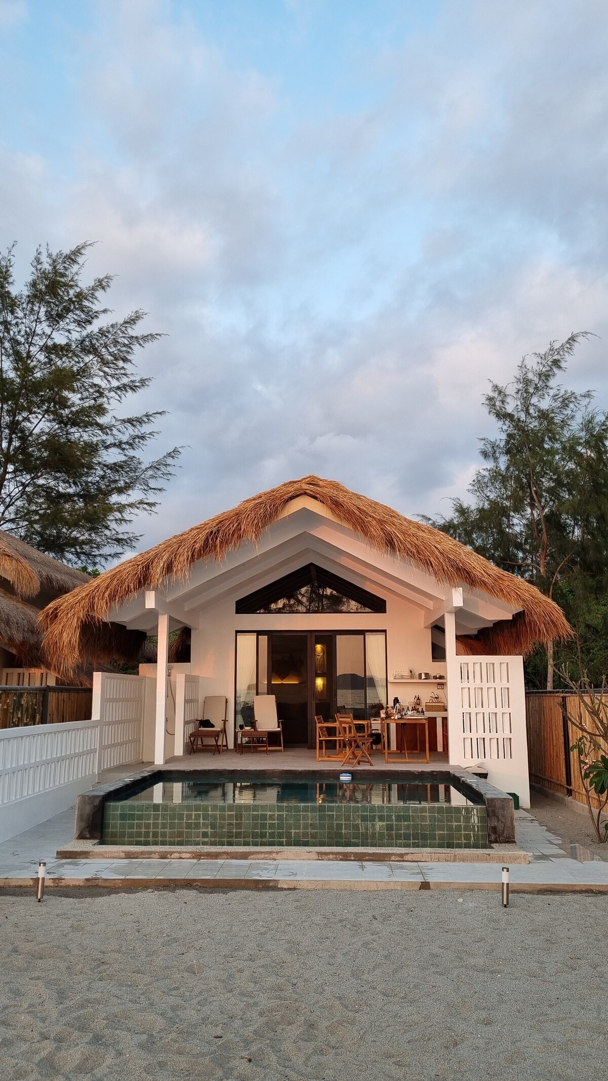 Villa front view with thatched roof and pool from beach at twilight